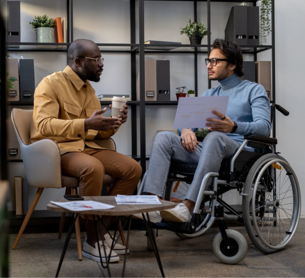 Two men, one of them in a wheelchair, casually talking about work.